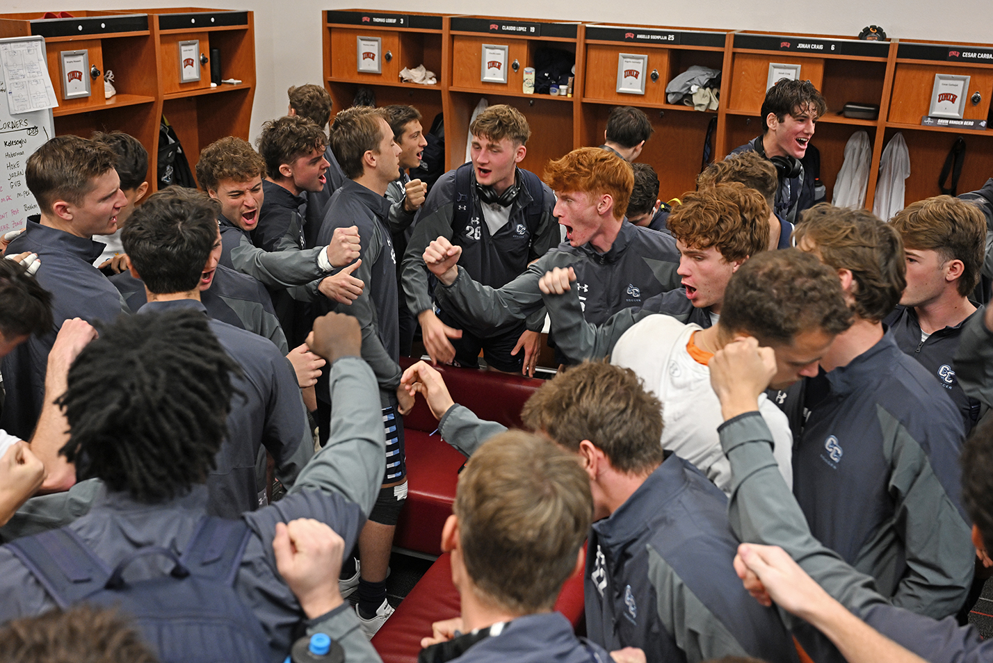 A soccer team gives a cheer as they huddle in the locker room.