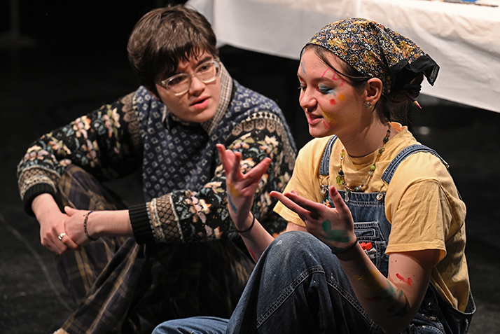 one actor gestures while speaking to another actor while seated on the floor