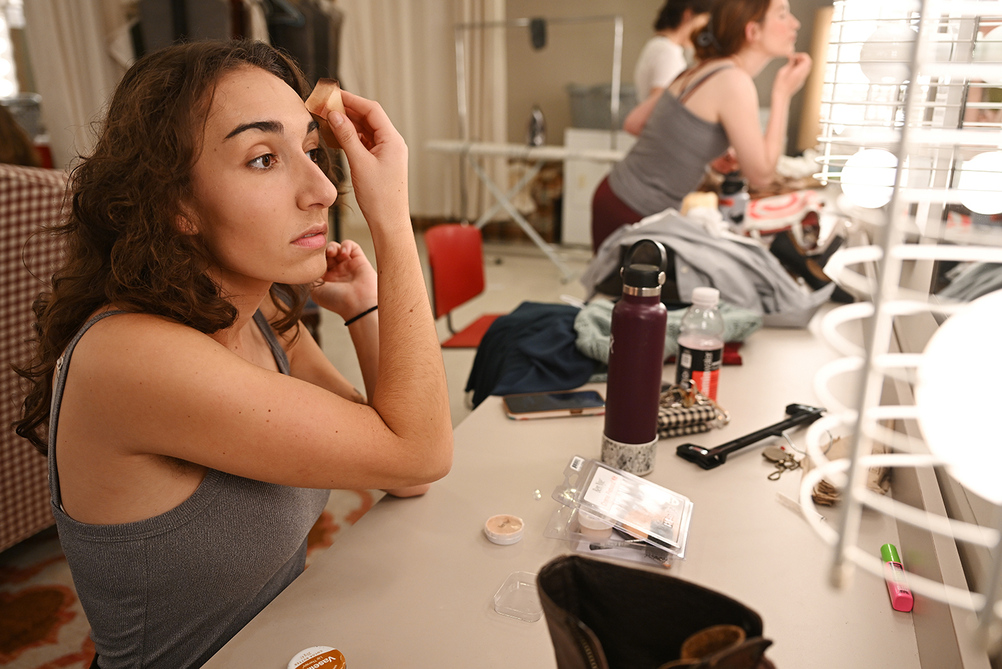 An actor does her makeup in a dressing room mirror.