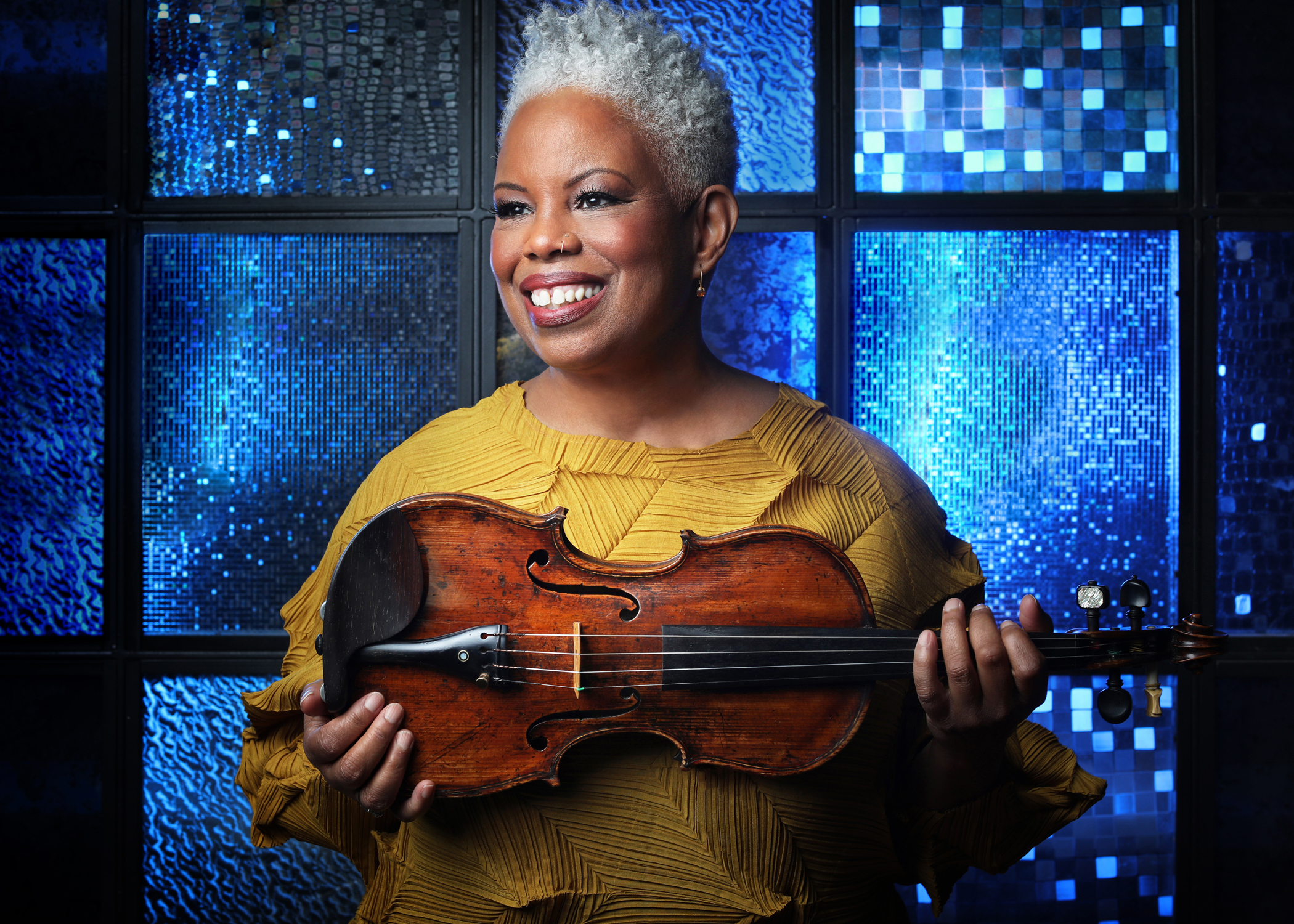 Regina Carter with her violin in front of blue stained-glass window