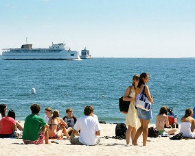 Connecticut College students on Ocean Beach, with the ferry and lighthouse in the background.